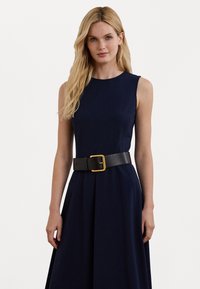 Vestido sem mangas azul-marinho com saia rodada e um cinto largo preto com fivela dourada, criando uma silhueta estruturada.