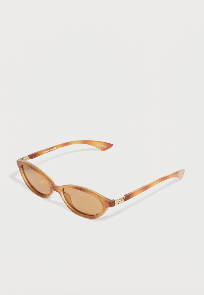Lunettes de soleil ovales marron avec montures translucides et verres teintés assortis, reposant sur une surface blanche.