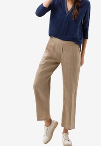 Pantalon en lin beige à coupe décontractée avec plis devant, associé à un haut à manches longues bleu marine et des baskets blanches.