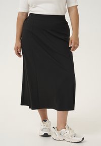 Zwarte midi-rok van gladde stof met een aansluitende tailleband en zijzakken, gecombineerd met witte sportschoenen.