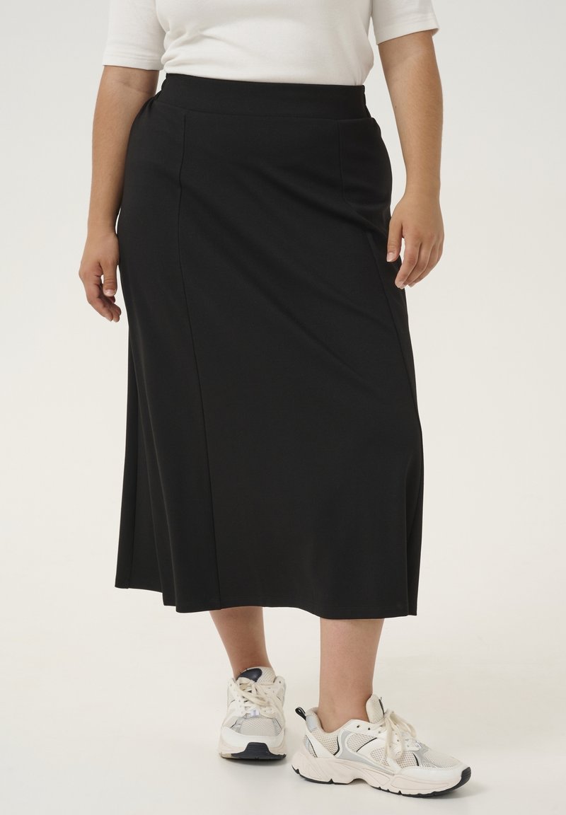 Zwarte midi-rok van gladde stof met een aansluitende tailleband en zijzakken, gecombineerd met witte sportschoenen.