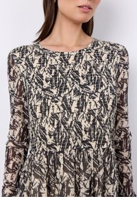 Langärmliges Kleid mit einem abstrakten Muster in Schwarz und Creme, einem strukturierten Oberteil und einem mehrlagigen Rock aus leichtem Stoff.