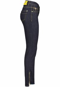Cienkie dżinsy w ciemnym denimu z żółtymi akcentami; posiadają boczny zamek przy kostce i tradycyjny krój pięciu kieszeni.