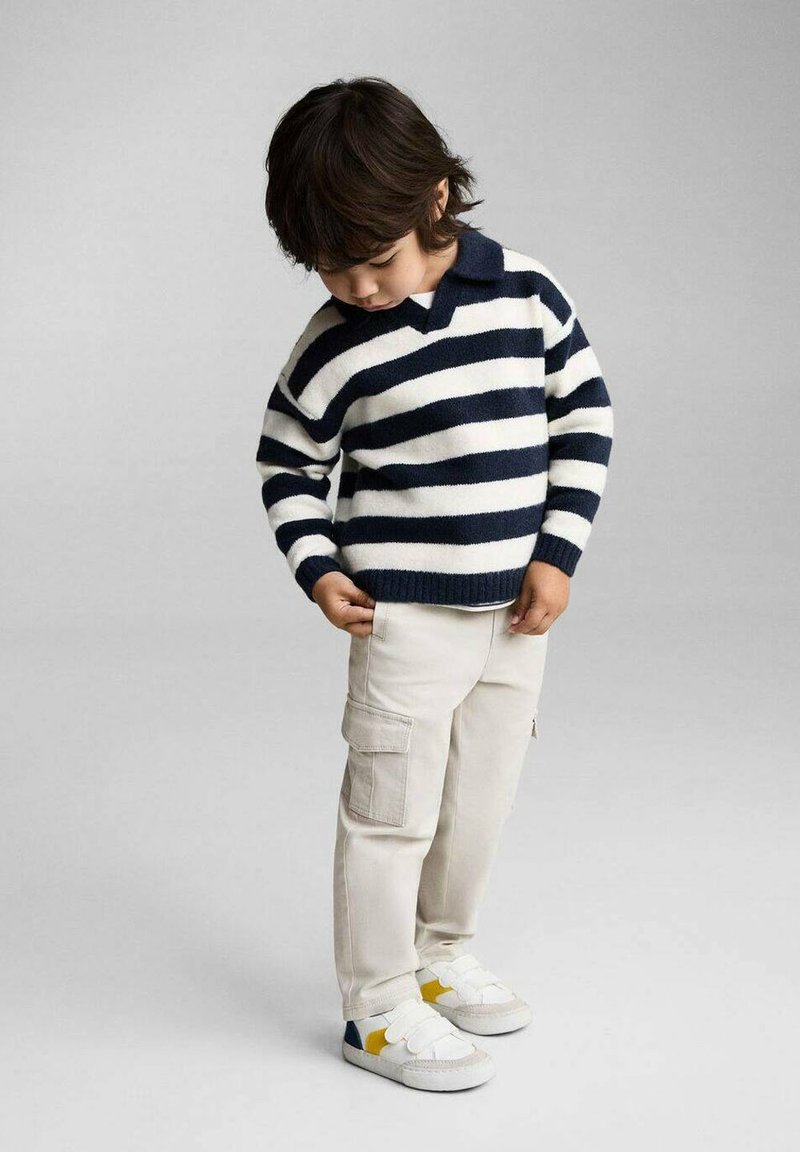 Barn iført en navy og hvid stribet sweater med krave, beige cargobukser og hvide sneakers med gule og blå accenter.
