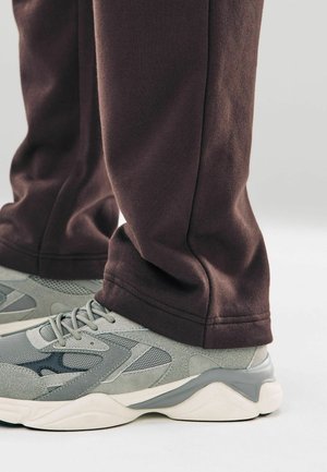 Gray athletic shoes with mesh and suede accents, paired with relaxed-fit dark brown sweatpants, showing hems and fabric texture.