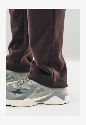 Hallid hallid spordijalanõud, millel on võrgud ja nahamuudatused, koos mugavate tumedate pruunide spordipükstega, näidates ääri ja kangast tekstuuri.