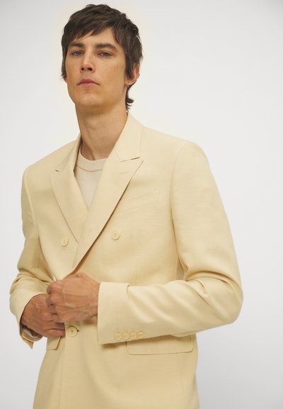 Lichtbeige dubbelzijdige blazer met een notch-lapel, twee knopen en een enkele borstzak, gepaard met een crèmekleurig T-shirt met ronde hals.