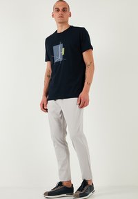 Marineblauwe katoenen t-shirt met een geometrische grafiek in blauw en groen. Gecombineerd met lichtgrijze slim-fit broek en zwarte sneakers.