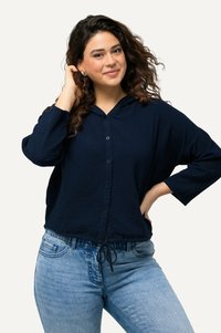 Navy-blaues, kapuzenförmiges Button-Up-Oberteil aus strukturiertem Stoff mit 3/4-Ärmeln und einem Kordelzugsaum, kombiniert mit hellblauen Jeans.