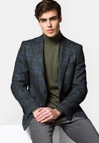 Kurtka w kratkę w ciemnozielonym i granatowym kolorze, mieszanka wełny, jednorzędowa z dwoma guzikami, zestawiona z dopasowanym oliwkowym golfem i szarymi spodniami.