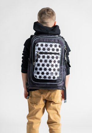 Zaino con motivo esagonale nero e grigio, dotato di tasca frontale con zip, spallacci regolabili e schienale imbottito, indossato da un bambino.