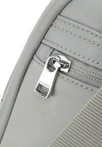 Grå tygsrynge med en slät textur, en silverfärgad dragkedja med "BOGNER" ingraverat, och vertikalt sydda detaljer på sidan.