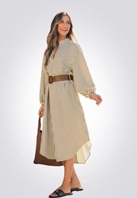 Robe midi rayée en crème et marron avec un col, des manches bouffantes et une taille ceinturée. Associée à un sac en osier et des sandales à glisser.