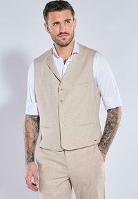 Beige Leinen-Mischung Weste mit schmalem Schnitt, Reverskragen, Fünfknopfverschluss und zwei Fronttaschen, kombiniert mit einem weißen Hemd.