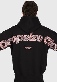 Person wearing a black hoodie with "Dropsize Co." in leopard print letters and "For Hustlers Est. 2020" text on the back.