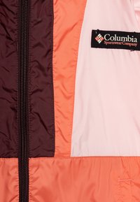 Barvit jakna Columbia Sportswear s paneli v temno rjavi, koralni in svetlo roza barvi, z zadrgo in blagovno oznako na strani.