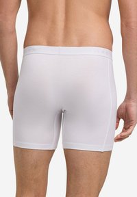 Weiße Baumwoll-Boxershorts mit glatter Textur und elastischem Bund, der eine dezente Markierung aufweist. Eng geschnitten für eine bequeme Passform an den Oberschenkeln.