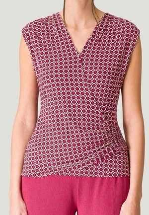 Kvinde iført ærmeløs, V-hals, mønstret pink top med rynkeeffekt på højre side og ensfarvede pink bukser.