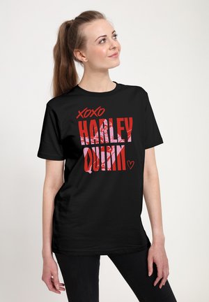 Ung kvinde med hestehale iført sort T-shirt med teksten "XOXO Harley Quinn" i røde bogstaver og et lyserødt grafik bag teksten.