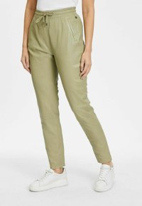 Licht olijfgroene tapered broek met een trekkoord in de taille, zijzakken en een gladde textuur, gecombineerd met witte sportieve sneakers.