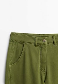 Pantalon taille haute vert olive avec poches avant, passants de ceinture et fermeture par bouton métallique sur fond blanc.