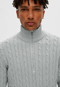Hellgrauer Strickpullover mit hohem Kragen, Reißverschluss und Zopfmuster mit geripptem Textur, der eine enge Passform bietet.
