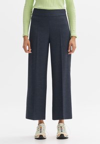 Pantalons navy à jambes larges en tissu texturé avec une taille haute, associés à des baskets légères et sportives. Les plis verticaux renforcent la structure.