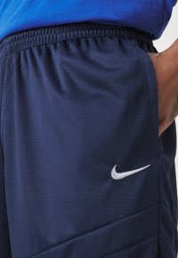 Námorné športové šortky s textúrovaným materiálom, elastickým pásom a bielym logom Nike na dolnej ľavej strane.
