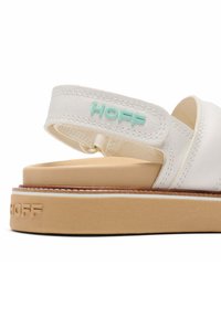 Sandalia de cuero blanco con correa ajustable, suela de goma tostada y marca en relieve. Presenta acentos de azul claro en la correa.