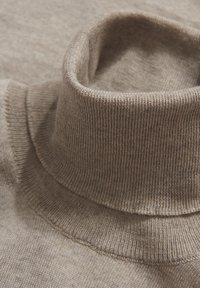 Beige turtleneck sweater i stof med ribbet tekstur, der har en høj krave og pæne syninger langs kanterne.
