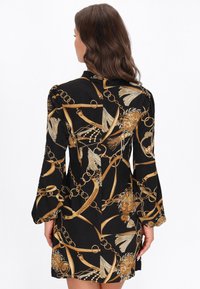 Fekete ruha aranylánccal és virágmintával, hosszú ujjakkal, strukturált kialakítással és sima szövettextúrával.
