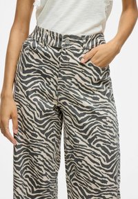 Beige ja tummanharmaan värisiä, zebra-kuosisia leveälahkeisia housuja, joissa on korkea vyötärö, etutasku ja nappikiinnitys.