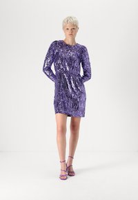 Vestido roxo de lantejoulas com mangas longas, decote barco e silhueta justa. Combinado com saltos com tiras no tornozelo em roxo. Fundo minimalista.