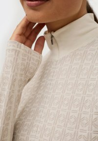 Licht beige kwart-rits top met geometrisch patroon. Voorzien van een hoge kraag en textuur lange mouwen. Zacht materiaal met fijne stikdetails.