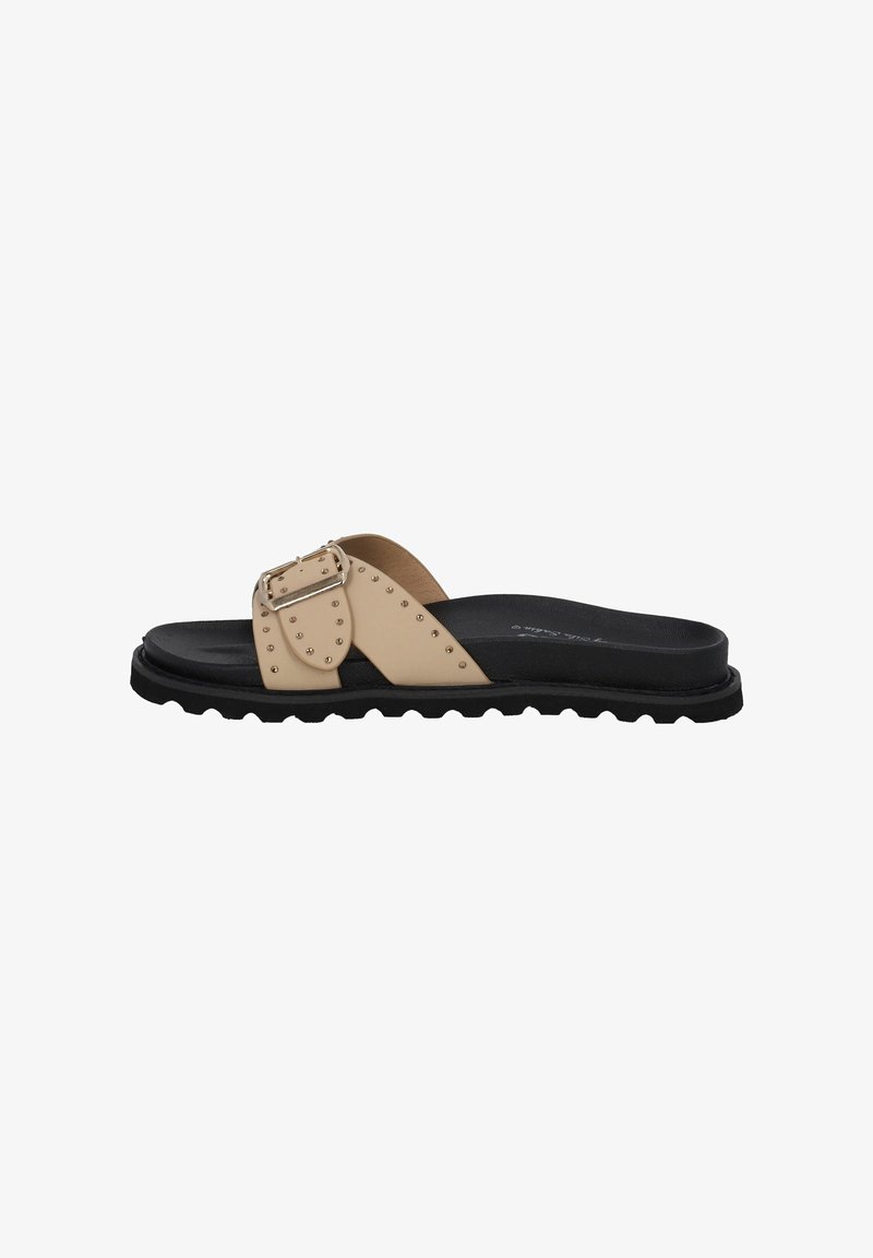 Beige slidesandal med en bred rem med metalliske nitter og en spænde, placeret på en sort tekstureret sål med bølgemønster.