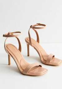 Nude patenten leren hoge hak sandalen met een vierkante neus, enkelbandjes en een gladde afwerking. Beschikt over een slanke stilettohak.