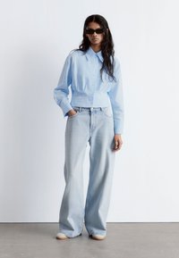 Light blue cropped button-up shirt paired with light blue wide-leg jeans. Smooth fabric with a relaxed fit. Minimalist design and no patterns.