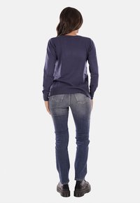 Maglietta a maniche lunghe blu marina con scollo tondo abbinata a jeans slim-fit blu e scarpe con platform nere. Texture liscia e design semplice.