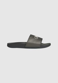 Zwarte slippers met een geperforeerde bovenzijde en een metalen accent. De zool is plat en ontworpen voor casual gebruik.