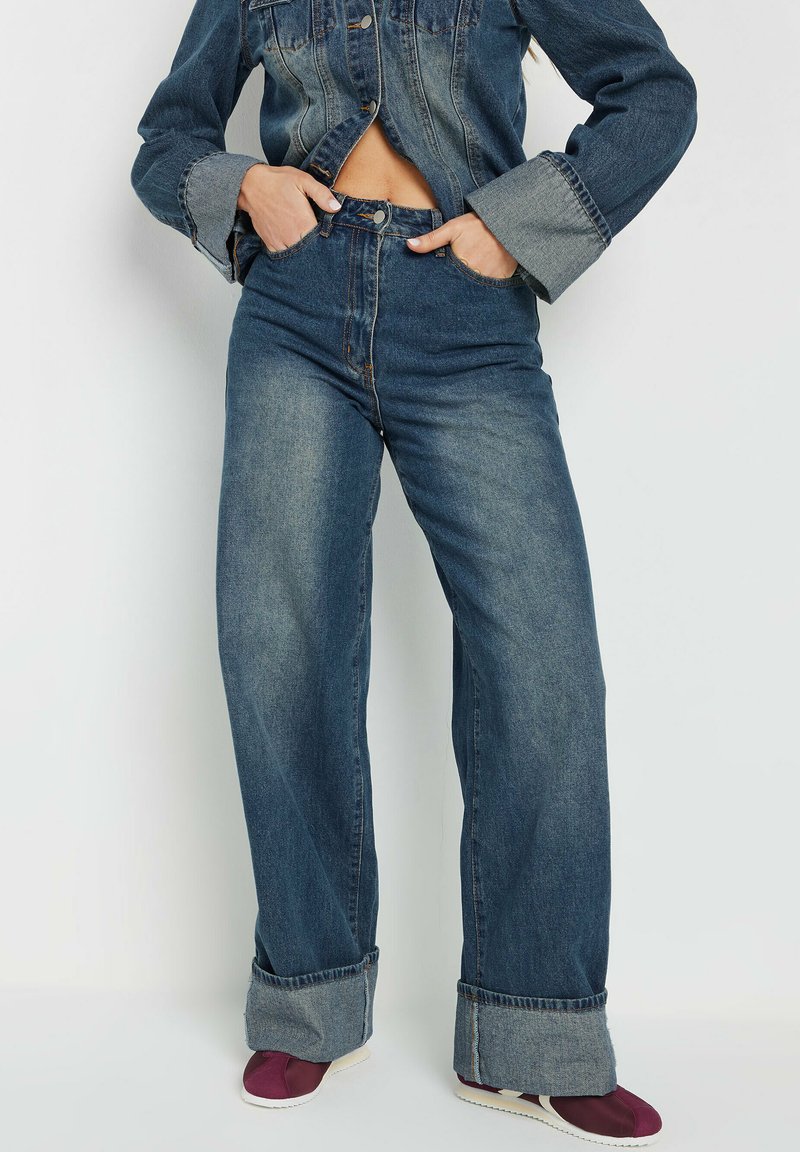 Hoge taille, wijdvallende jeans van donkerblauwe denim met lichte vervaging. Kenmerkt grote omslagen en een rits aan de voorkant met knoopsluiting.