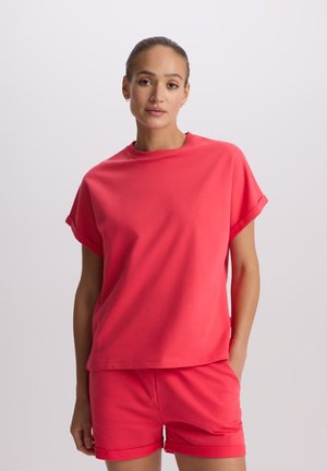 Jasnoróżowa bawełniana koszulka z krótkimi podwiniętymi rękawami i okrągłym dekoltem, w zestawieniu z dopasowanymi szortami. Prosty, nieskomplikowany design.