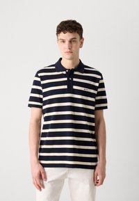 Marineblå og kremfarget stripete polo shirt med krage, korte ermer og logo på venstre bryst. Laget av teksturert bomullsstoff.