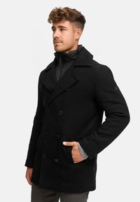 Schwarzer doppelt knöpfbarer Wollmantel mit großen Reverskragen, seitlichen Taschen und kontrastierenden grauen Strickbündchen. Glatte Textur und maßgeschneiderte Passform.