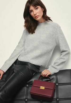 Szary, błyszczący sweter, czarne skórzane spodnie oraz bordowa torebka o sztywnej formie z złotą klamrą. Gładkie tekstury i wyraźne kształty.
