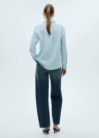 Blusa azzurra chiara a maniche lunghe con una vestibilità comoda e colletto a punta, abbinata a jeans dritti blu scuro a vita alta e tacchi neri.