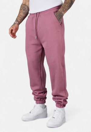 Rosa Jogginghosen mit einem elastischen Bund und Bündchen, ausgestattet mit Seitentaschen und einem Logo-Detail. Kombiniert mit weißen Sneakers.