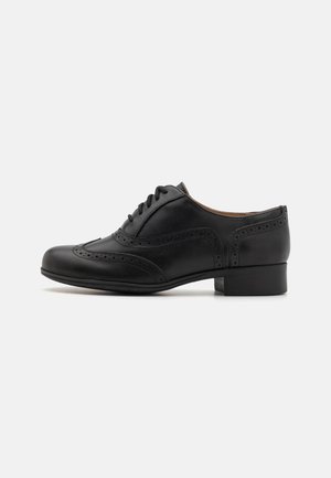 Zwarte leren oxford schoen met brogue-details, een ronde neus en een lage blokhak. Gladde textuur met een vetersluiting.