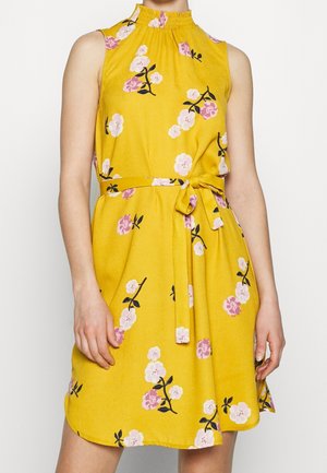 Žluté květované šaty s vysokým límcem, bez rukávů a s páskem na zavázání v pase. Vzory růžových a bílých květin na texturované látce.