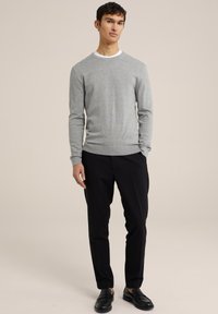 Suéter gris hecho de suave tejido de punto con cuello redondo, combinado con pantalones negros y mocasines negros, creando un look casual.