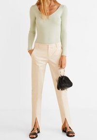Světle zelený žebrovaný top s dlouhým rukávem, spárovaný s béžovými kalhotami s bočními rozparky. Černá texturovaná taška a černé sandály dotvářejí vzhled.